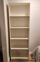 Full front view of the white veneer Ikea bookcase showing five shelves in a vertical rectangular frame.