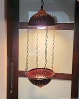 Photo of the ceramic hanging planter and lamp combo suspended and lit, showing the design and pendant style with chain