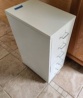 Side view of white metal filing cabinet with six drawers and caster wheels, showing clean white finish and handles
