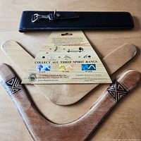 Photo showing black leather case for the metal slide ruler and two wooden boomerangs with packaging backing for one boomerang in background.