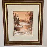 Framed oil painting showing a winter landscape with evergreen trees and a river, signature visible.
