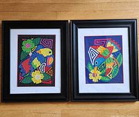 Both framed Panama Mola artworks side by side on floor: colorful birds, flowers, and abstract designs in hand-stitched textile art with black frames.