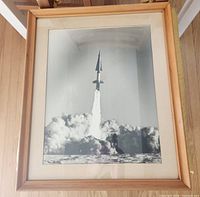 Photo of framed vintage rocket launch photograph showing full frame and matting against a wooden floor.