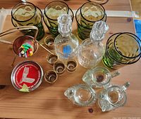 Photo showing vintage green glasses with bubble texture, two clear glass bottles with stoppers, mini gold shot glasses, bar toothpicks in holder, and UN coasters.