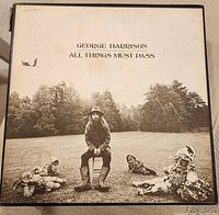 Front cover of George Harrison's All Things Must Pass vinyl record album showing seated figure with forest background.