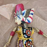 Close-up of the puppet's head and upper body showing detailed painted face, headpiece, and decorative fabric costume with floral designs and yellow thread accents.