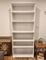 Full front view of the white solid wood Ikea bookcase showing five adjustable shelves.