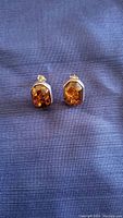 Pair of silver stud earrings with genuine amber stones on blue fabric background.