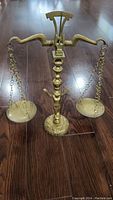 Full view of the brass balance scale showing the two hanging pans and base figurine.