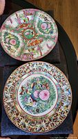 Two 10-inch decorative plates with Asian themes laid on a surface, showing overall designs and colors.