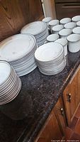 Overview of the full set of porcelain dishes arranged on counter including plates, small plates, bowls, and cups