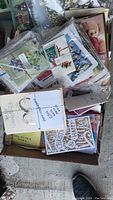 Box of various greeting cards including some holiday-themed cards like Christmas with envelopes and plastic sleeves visible.