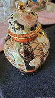 Full view of Japanese vase with lid and gold accents on wooden stand