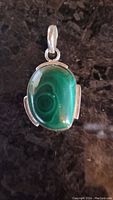 Front view of polished malachite pendant in sterling silver on a dark surface.