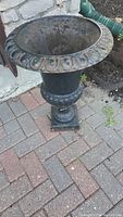 Full view of metal planter standing on brick pavement showing shape and decorative rim.