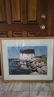 Full view of the professionally framed print showing coastal scene with white house and dock.