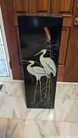 Front view of the tall black lacquer pedestal with white birds painted on it, showing two birds and botanical details.