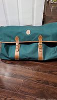 Front view of green Polo weekender duffle bag with closed flap showing leather buckle straps and Polo logo patch.