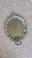 Top-down photo of oval silver plated tray showing its detailed scalloped rim and ornate handle at one end.