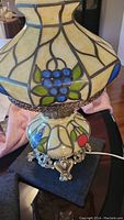 Full view of lamp showing stained glass shade and base with grape motif and ornate metal feet.