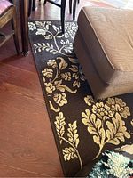 Close-up of brown area rug with tan and cream floral pattern beneath furniture on hardwood floor.