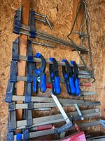 Overall photo showing the full assortment of clamps on a wooden background wall, various sizes and types visible.