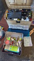 Open view of large and small tackle boxes with gloves on top and assorted lures inside.