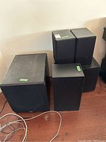 Five black Paradigm speakers on hardwood floor: one large sub-like box, two bookshelf monitors, one center channel and one tall speaker