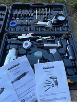 Full view of open tool carrying case with pneumatic tools, attachments, manuals, and accessories organized inside.