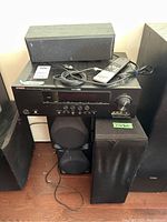 Front and angled view of Yamaha HTR-6240 receiver stacked with speakers. Remote and cords placed on top. Shows black finish and control buttons on receiver, along with several black Yamaha speakers around it.