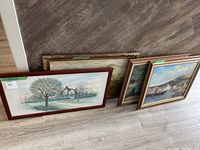 Four framed landscape pictures leaning against the wall on the floor, showing various scenes including houses and boats.