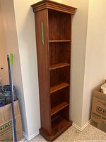 Angled side view of the tall wooden bookcase showing the five fixed shelves and crown molding top.