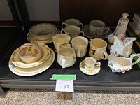 Multiple ceramic dishware items displayed on shelf including Bunnykins themed plates, bowl, mugs, cups, and decorative figurines.