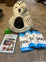 Owl-shaped cat house, poo bag boxes, green bell toy, and 'Cat Behavior and Training' book