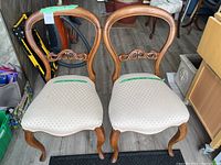 Two wooden balloon back chairs with beige patterned upholstered seats shown from front.