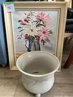 Framed floral oil painting resting behind ceramic plant pot on floor.