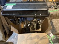 Mastercraft drill press viewed from above inside a cardboard box, showing motor housing and drill head.