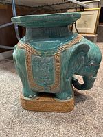 Side view of the green glazed clay garden stool shaped like an elephant with detailed carvings including a floral saddle and patterned borders on the body.