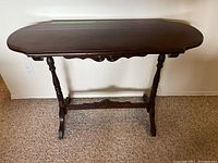Front view of the wood hall table, showing scalloped oval tabletop, turned legs, and carved apron details.
