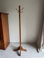 Full view of wood hall tree standing upright near a wooden cabinet and curtains