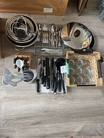 Full view of various kitchen utensils including metal bowls, flatware, utensil block, cooking pan with glass lid, and a basket holding glasses.