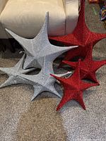 Six ornamental stars displayed on carpet next to couch. Three silver stars and three red stars in various sizes.