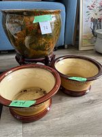 Front view of the large floral plant pot on wooden stand alongside two smaller round ceramic plant pots, showing overall set condition and design.
