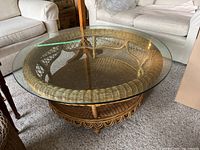 Overall angled view showing round rattan coffee table with clear glass top resting on woven rattan base.