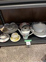 Display of assorted teacups, saucers, teapot, and serving dishes arranged on shelf