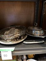 Shelf display showing silver plated serving tray, cutlery set in plastic bag, and covered serving dish