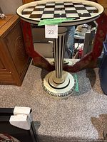 Photo of the entire pedestal table showing its checkerboard top, cylindrical pedestal with vertical stripes, and round base with Greek key pattern.