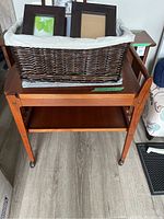 Wicker basket on trolley shelf containing photo frames and linens