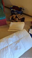 View of the full lot including white down comforter, cream crocheted blanket, moose-themed quilt and laundry basket.