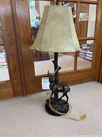 Full view of bronze buck table lamp with beige fabric shade in front of glass door.